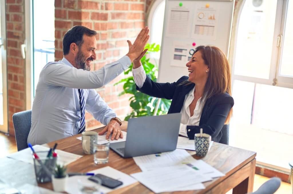 Two middle age business workers smiling happy and confident. Working together with smile on face hand giving high five at the office